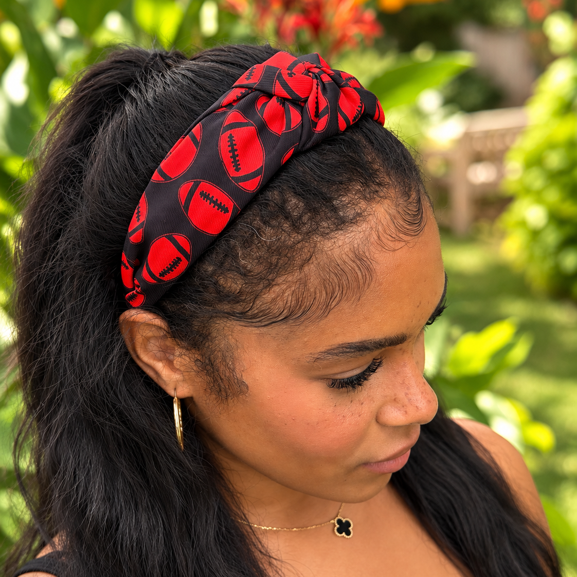 A woman wearing a red and black patterned fabric headband with football motifs, photographed outdoors in a garden setting.